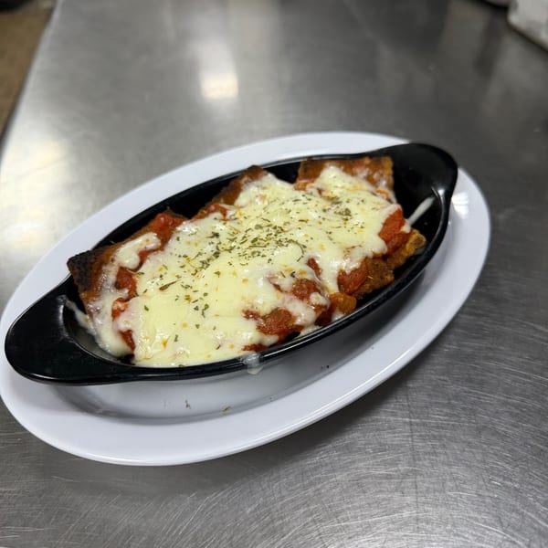 Snazzy's Hot Wings' cheesy chicken parmesan in a black dish on a white plate.