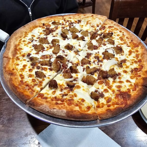 A whole pizza with white sauce, sausage, and onions on a metal pan.