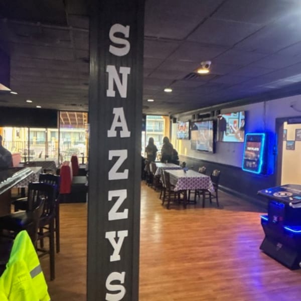 Interior of Snazzy's Hot Wings, featuring a bar, dining tables, TVs, and a glowing blue jukebox.