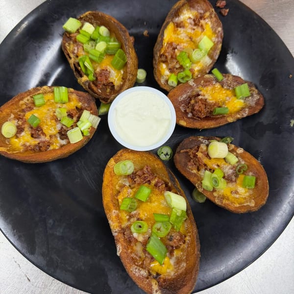 Five loaded potato skins with melted cheese, ground meat, and green onions, arranged around a dip.