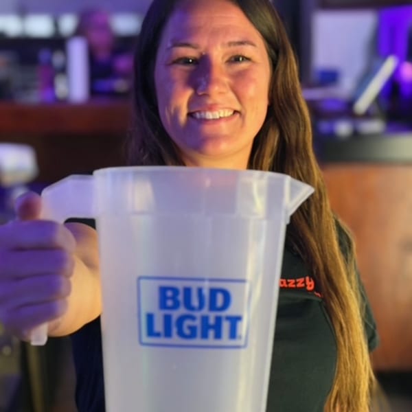 Smiling woman holding a Bud Light pitcher, wearing a Snazzy's Hot Wings shirt.