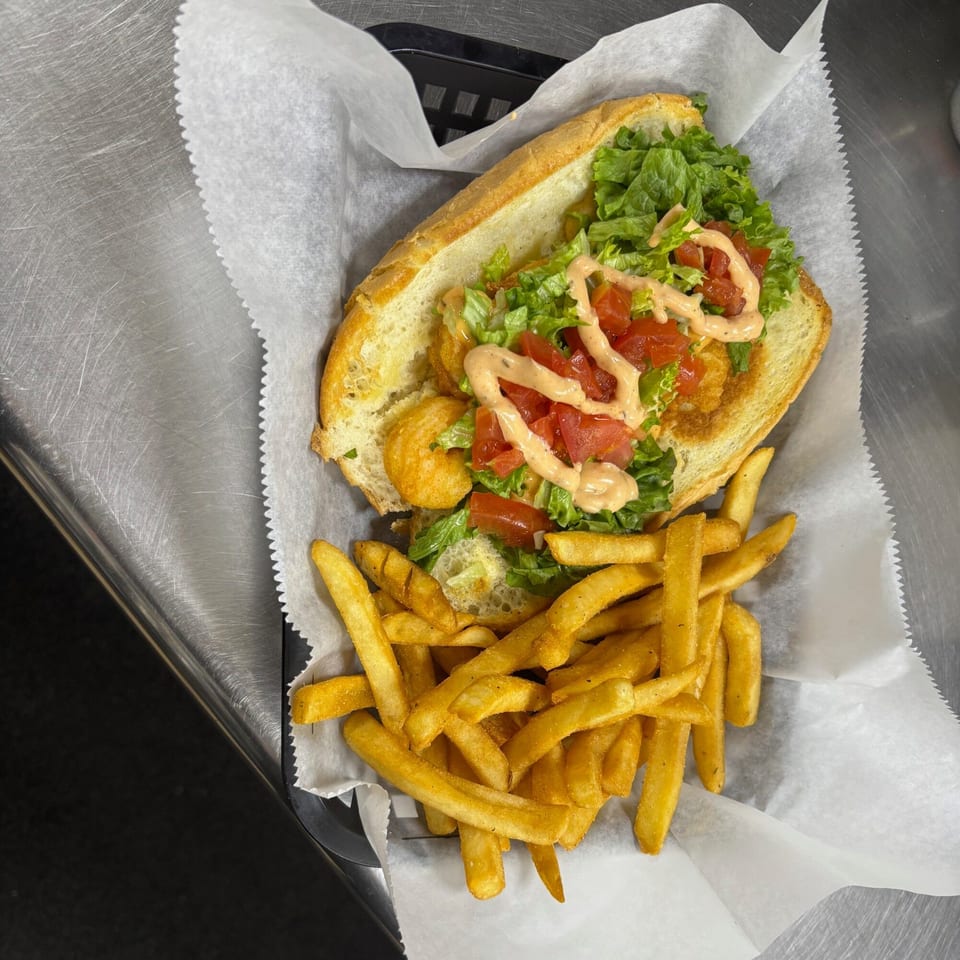 A Snazzy's Hot Wings shrimp po'boy with lettuce, tomatoes, and sauce, served with fries.