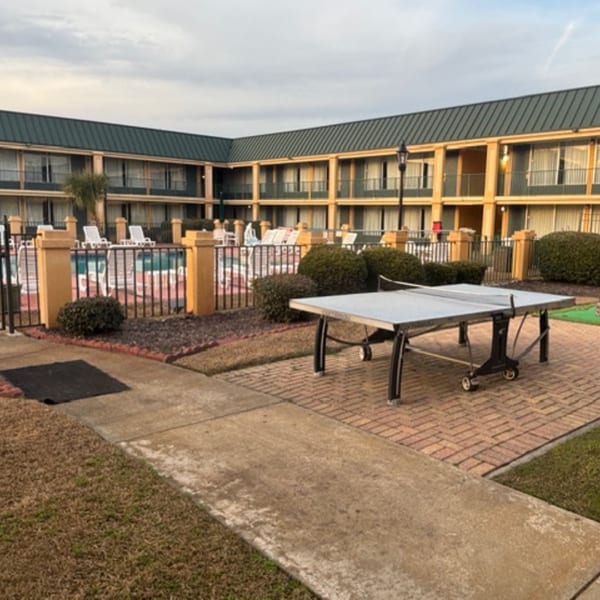 An outdoor ping pong table on a brick patio next to a hotel building with a pool.