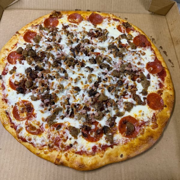 A whole meat lover's pizza with pepperoni, sausage, and ham in a cardboard box.