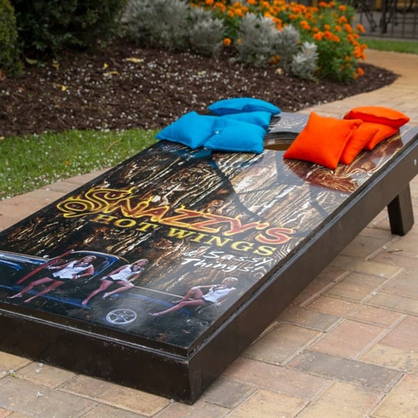 Snazzy's Hot Wings branded cornhole board with blue and orange beanbags on a patio.