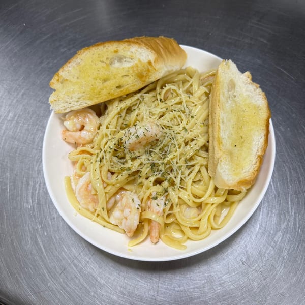 Shrimp linguine pasta with parmesan cheese, herbs, and two slices of garlic bread on a white plate.