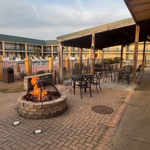 Outdoor patio with a fire pit, tables, chairs, and a pool in the background.