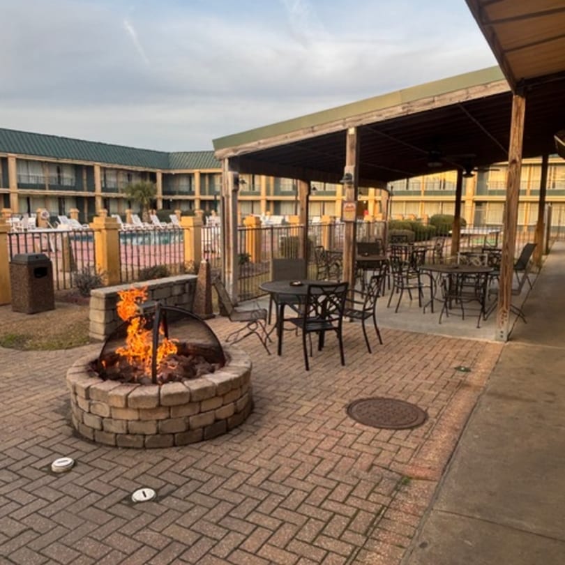 Outdoor patio with a fire pit, tables, chairs, and a pool in the background.