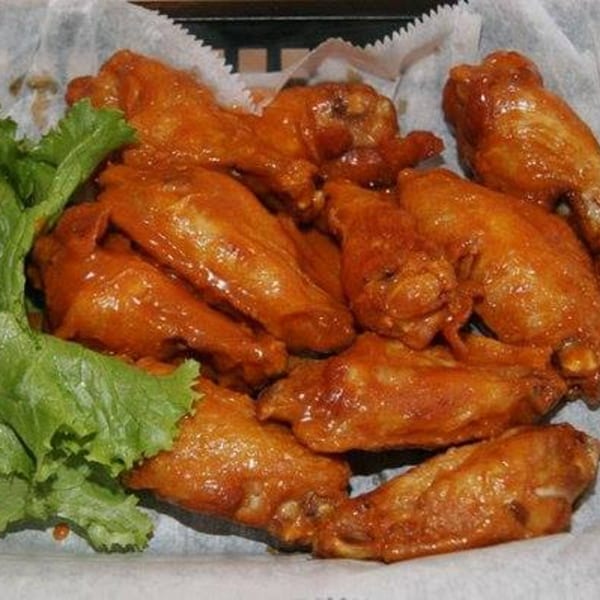 A basket of Snazzy's Hot Wings, glistening with sauce, served with a side of fresh lettuce.