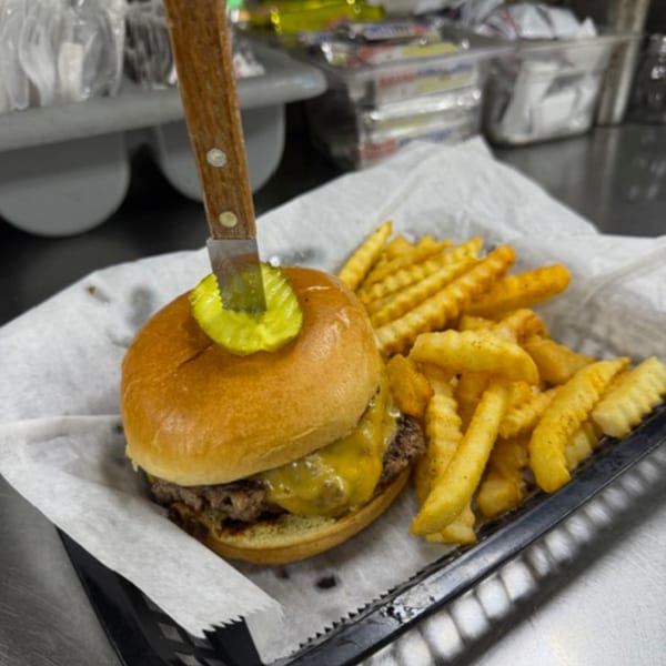 Cheeseburger with a pickle and knife, served with crinkle-cut fries in a basket.