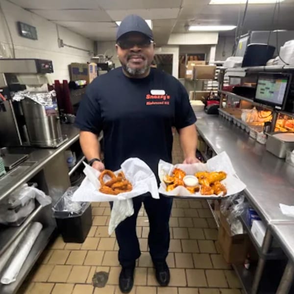 A Snazzy's Hot Wings employee in a kitchen holds trays of onion rings and buffalo wings.