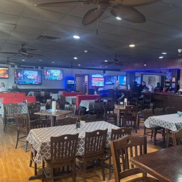 Interior of Snazzy's Hot Wings with dining tables, red booths, a bar, and multiple TVs.