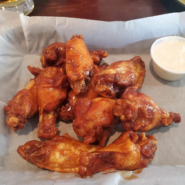 A basket of Snazzy's Hot Wings, coated in a glossy red sauce, with a side of ranch.